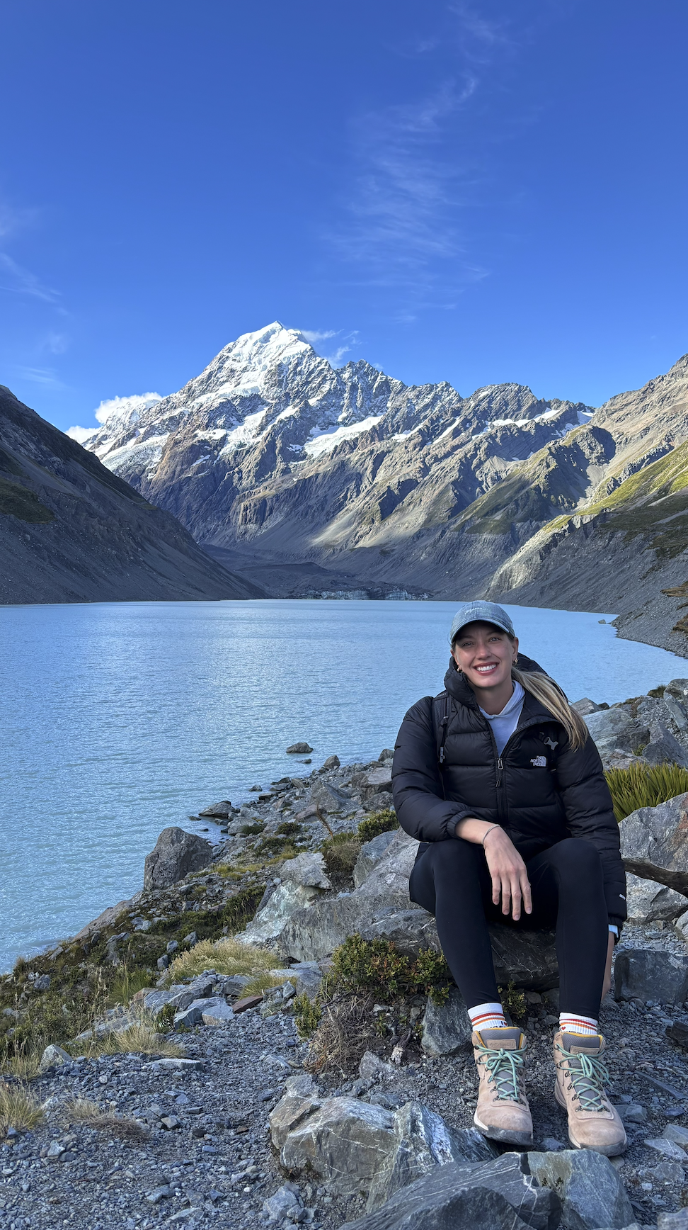 Hiker sitting by alpine lake with Tasman Glacier New Zealand