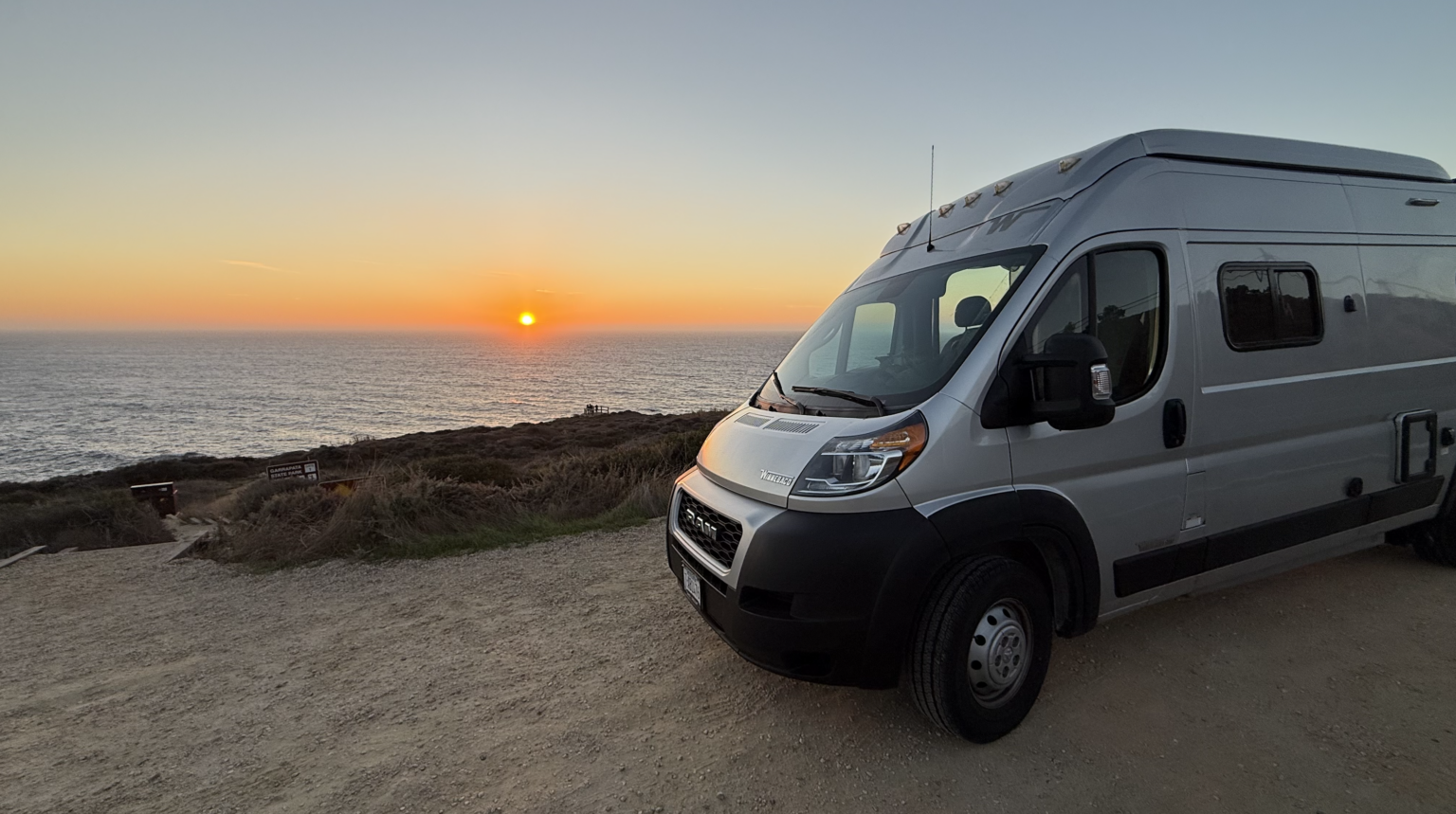 A campervan parked on a clifftop overlooking the Pacific Ocean at sunset along the Big Sur coastline
